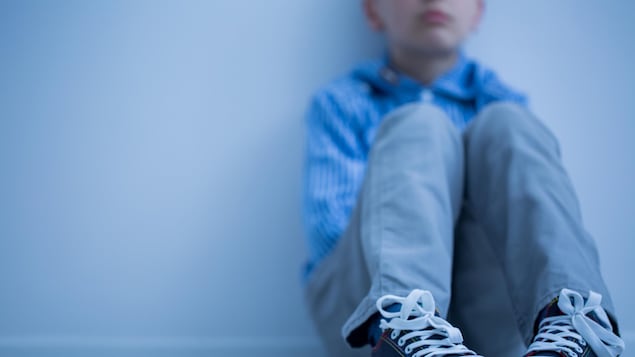 Un enfant dont on ne voit pas le visage est assis par terre.
