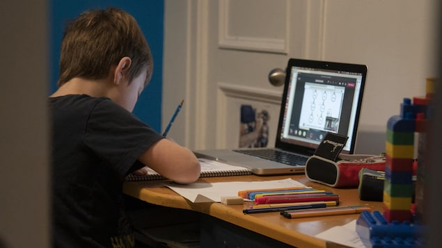 Un jeune garçon fait ses devoirs devant un écran d'ordinateur.