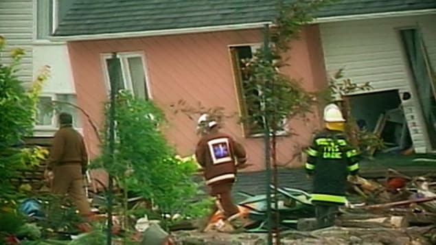 Une maison a moitié effondrée avec des pompiers autour.
