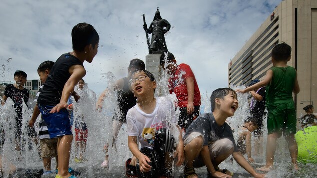 Une dizaine d'enfants, dont l'un portant des lunettes, jouent dans des jets d'eau sortant du sol lors d'une journée de canicule à Séoul, en Corée du Sud. Une dizaine d'enfants, dont l'un portant des lunettes, jouent dans des jets d'eau sortant du sol lors d'une journée de canicule à Séoul, en Corée du Sud.