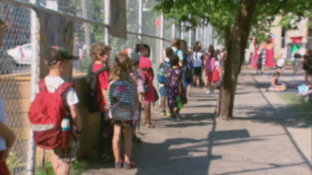 Plusieurs élèves avec leur sac à dos et leurs vêtements d'été, le long d'une clôture d'école