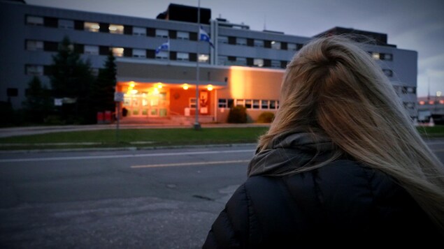 Une femme se tient debout devant un hôpital. 