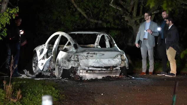 Des enquêteurs pointent leur lampe de poche vers la carcasse du véhicule incendié la nuit.