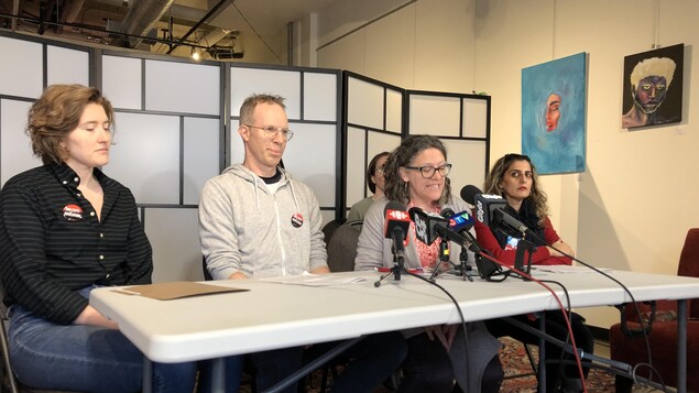 Des personnes attablés devant des micros de journalistes dans une salle.