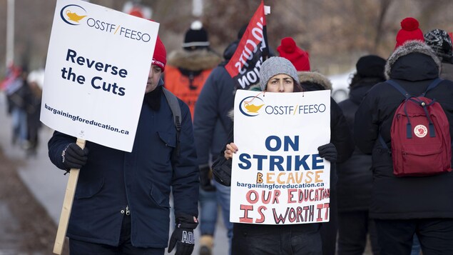 Des grévistes marchent et brandissent des pancartes qui dénoncent les compressions en éducation.