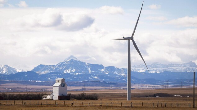 Paysage du sud de l'Alberta avec une éolienne en premier plan à côté d'un ascenseur à grain et les montagnes Rocheuses en arrière-plan Paysage du sud de l'Alberta avec une éolienne en premier plan à côté d'un ascenseur à grain et les montagnes Rocheuses en arrière-plan