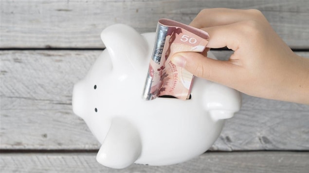 Une main glisse un billet de 50 $ dans une tirelire.
