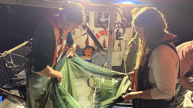 Deux personnes regardent dans un filet de pêche, la nuit sur un bateau.