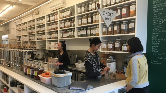 Au mur des étagères d'épices et deux employés sont derrière un comptoir avec une cliente qui effectue une commande au comptoir.