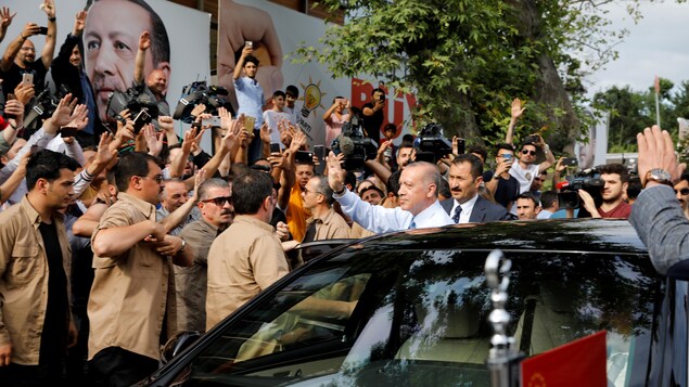 Erdogan se tient à côté de sa voiture entouré de gardes du corps et de gens qui le saluent. Erdogan se tient à côté de sa voiture entouré de gardes du corps et de gens qui le saluent.