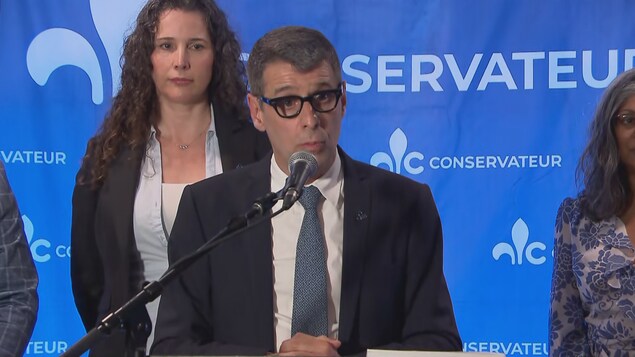 Éric Duhaime debout derrière un lutrin lors d'une conférence de presse avec ses candidats de la région de Québec.  