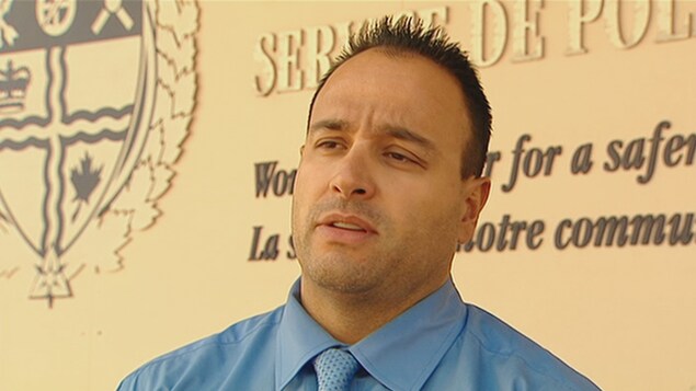 Un homme devant le logo du Service de police d'Ottawa.
