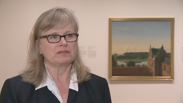 Une femme aux cheveux blonds portant des lunettes noires est debout près d'un tableau. Une femme aux cheveux blonds portant des lunettes noires est debout près d'un tableau.
