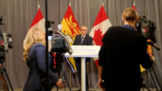 Un homme en habit parle devant plusieurs caméras en conférence de presse.