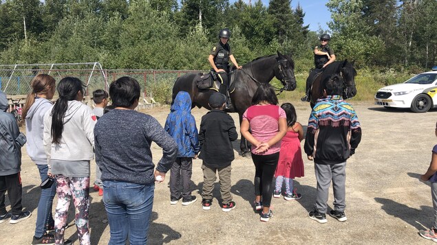Une dizaine d'enfants de dos admirent deux policières à cheval.