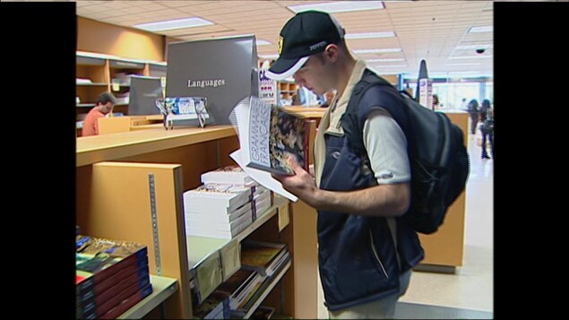 Un jeune homme dans une librairie tient une grammaire française dans ses mains dans le rayon Languages (écrit en anglais).