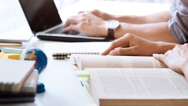 Des étudiants devant un ordinateur et un livre ouvert