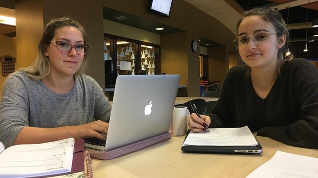 Deux étudiantes assises autour d'une table avec leurs ordinateurs.