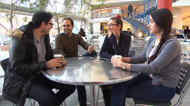 Quatre jeunes discutent autour d'une table dans ce qui semble être une cafétéria.
