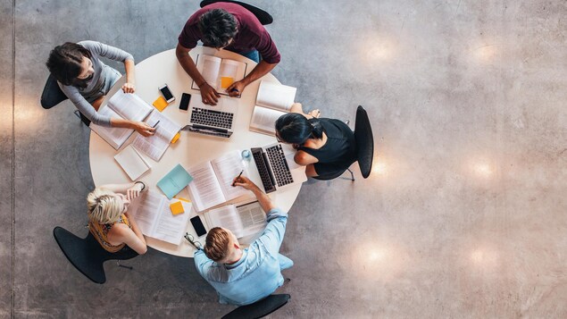 Des étudiantes et des étudiants assis autour d'une table avec leurs cahiers et ordinateurs.