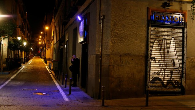 Un homme fume une cigarette seul dans une ruelle déserte.