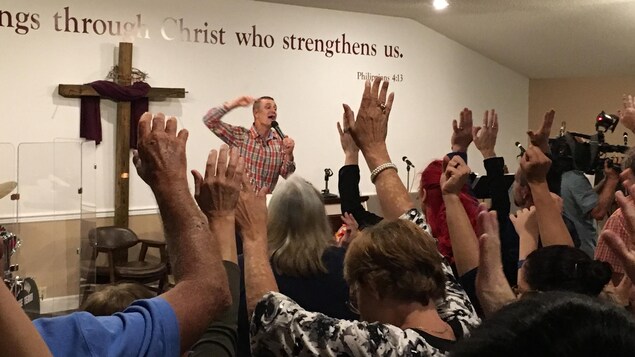 Des fidèles lèvent les mains dans les airs. Devant eux, un pasteur parle dans un micro.