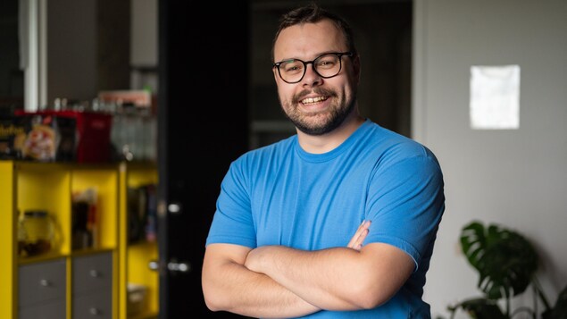 Un homme prend la pose, souriant, les bras croisés. 