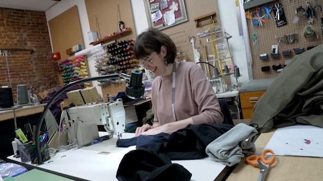 Une couturière sourit derrière sa machine à coudre dans son atelier. 