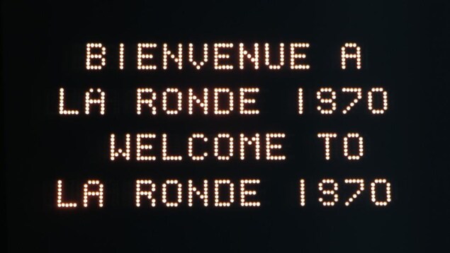Un panneau d'affichage lumineux indique « Bienvenue à la Ronde 1970, Welcome to La Ronde 1970 ». Un panneau d'affichage lumineux indique « Bienvenue à la Ronde 1970, Welcome to La Ronde 1970 ».