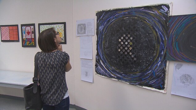 Une femme regarde une oeuvre exposée par l'organisme Les Impatients.