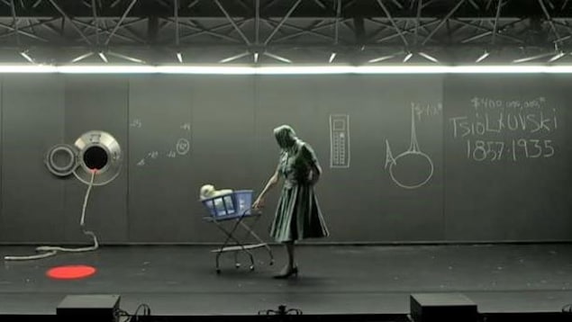 Une femme pousse un bébé dans un carrosse. Sur le mur derrière elle se trouve un dessin de la Terre et un hublot de vaisseau spatial.