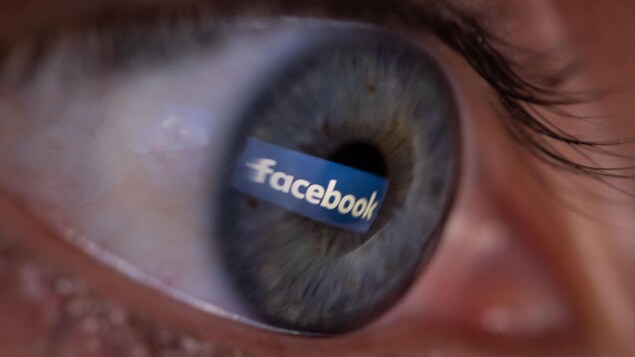 Un œil, vu de proche, avec la réflexion du logo de Facebook.