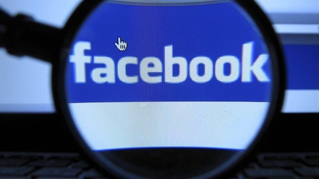 Une loupe grossit le logo de Facebook qui s'affiche sur un écran d'ordinateur.