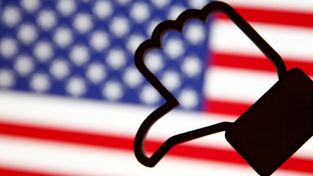 Un symbole Facebook «pouce vers le bas», devant un drapeau américain flou