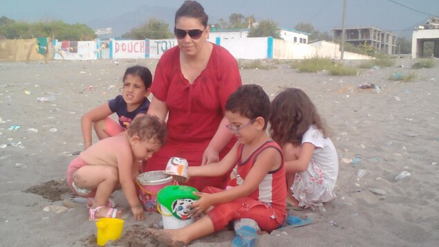 Une femme et quatre enfants sur une plage.