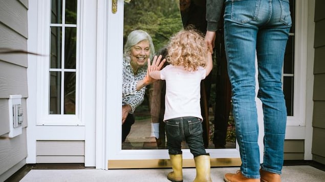 Une petite fille salue sa grand-mère par une fenêtre.