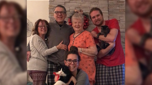 Une famille de quatre personnes avec une grand-maman au centre. Ils sont tous souriants.
