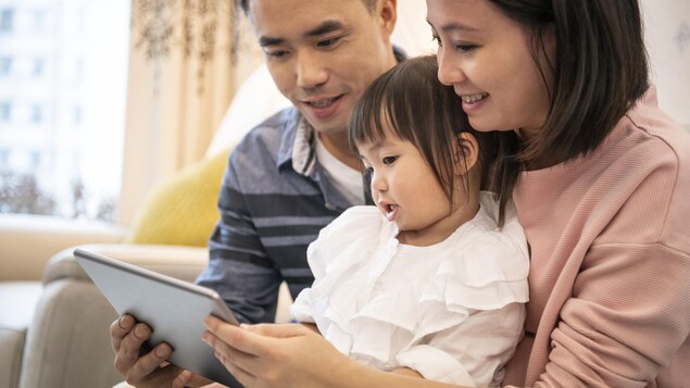 Des parents et leur fille écoutent un film sur une tablette.