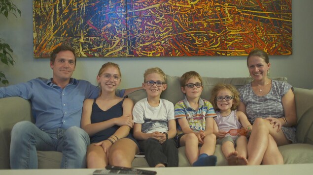 Le père est assis avec ses quatre enfants et avec Mélodie Chénier sur le divan. Le père est assis avec ses quatre enfants et avec Mélodie Chénier sur le divan.
