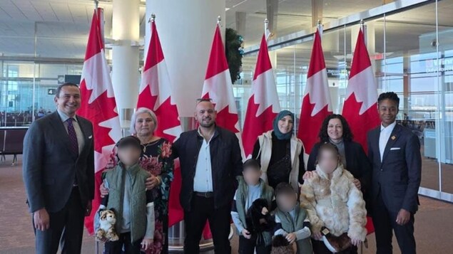 Des personnes dans un aéroport devant des drapeaux du Canada. 