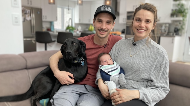 Les anciens patineurs de vitesse Samuel Girard et Kasandra Bradette sont assis sur leur divan en compagnie de leur poupon et de leur chien.