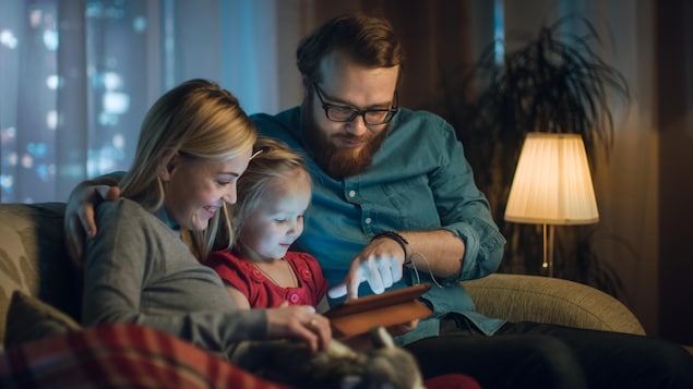 Une mère et un père regardent une tablette avec leur fille.