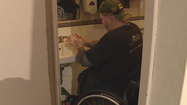 Un homme en fauteuil roulant se lave les mains dans la salle de toilette étroite d'un café Un homme en fauteuil roulant se lave les mains dans la salle de toilette étroite d'un café