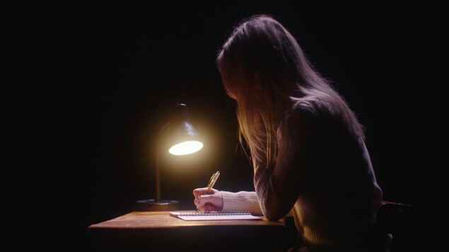 Une femme écrit dans un cahier près d'une lampe. 