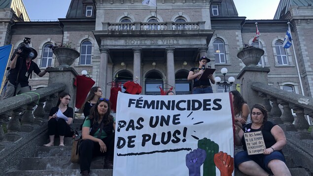 Des personnes avec une pancarte devant l'hôtel de ville de Sherbrooke.
