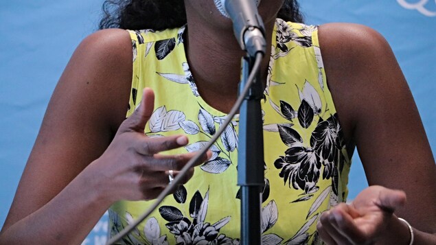 Une femme, dont on ne voit pas le visage, parle à un micro. Une femme, dont on ne voit pas le visage, parle à un micro.