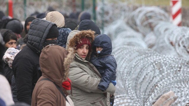 Une femme tient un bébé devant une barrière de barbelés.