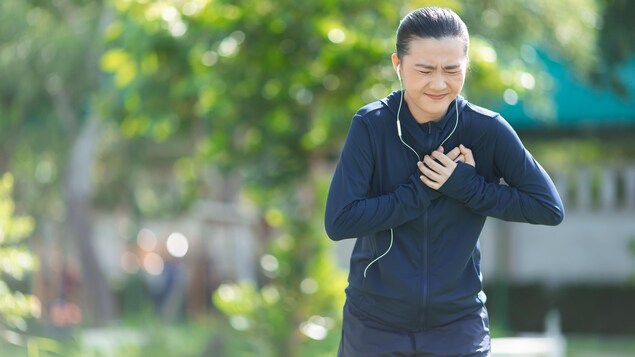 Une femme faisant de l'exercice dans un parc et souffrant de douleurs à la poitrine.