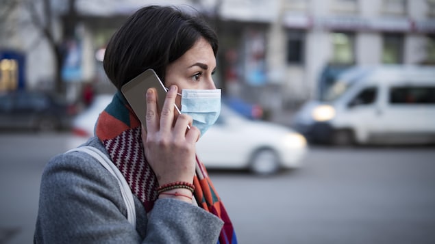 Une femme portant un masque marche dans la rue en parlant au téléphone.