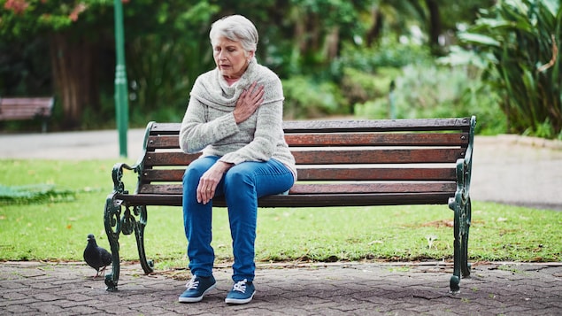 Une femme, assise sur un banc de parc, ne se sent pas bien. 